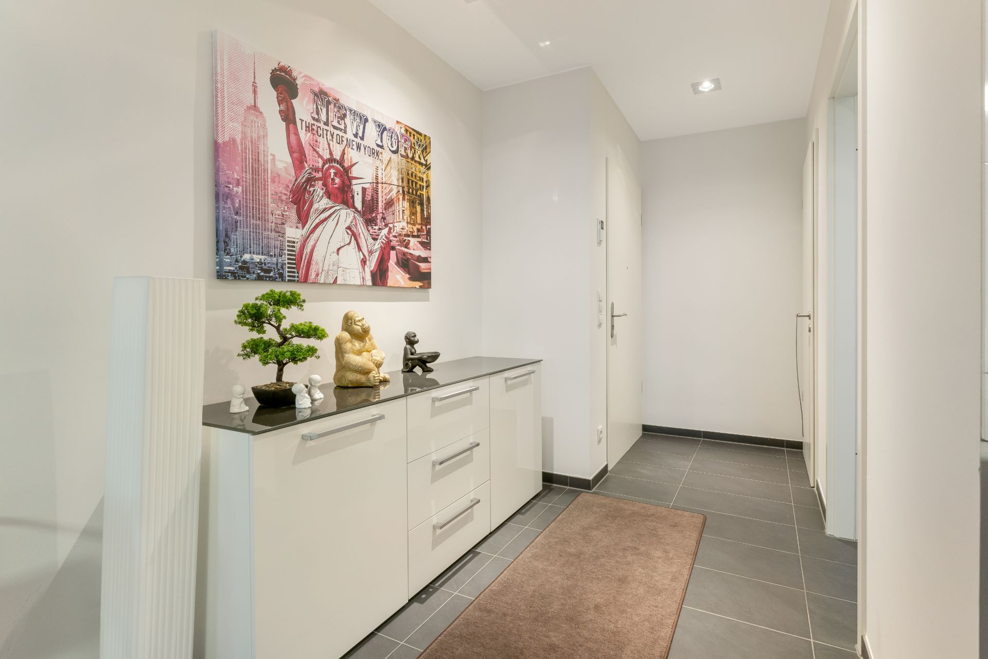 Heller Flur mit Sideboard, Dekorationen, Teppich und Bild an der Wand.