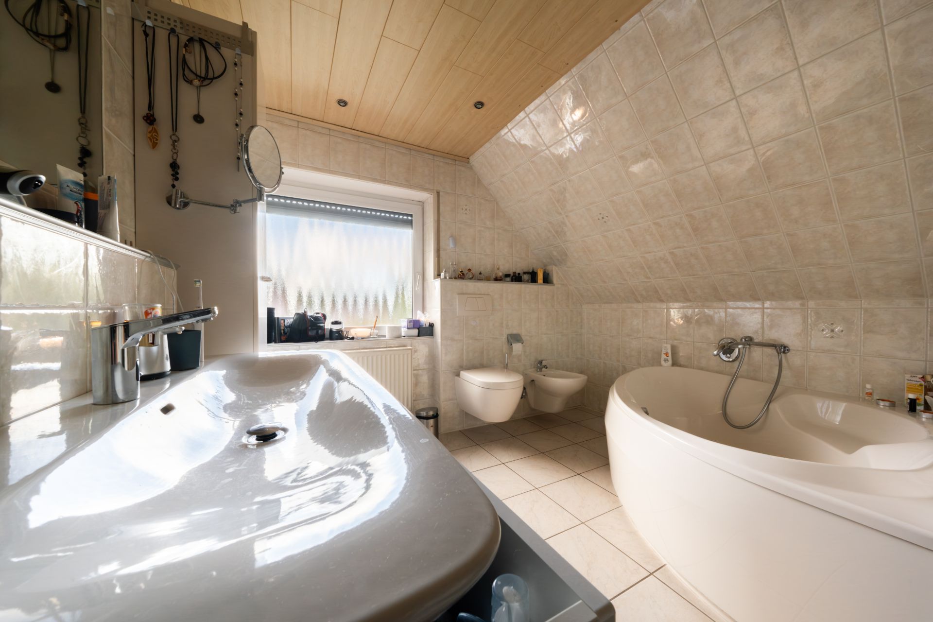 Modernes Badezimmer mit großem Waschbecken, Eckbadewanne, Bidet, Toilette und Fenster.