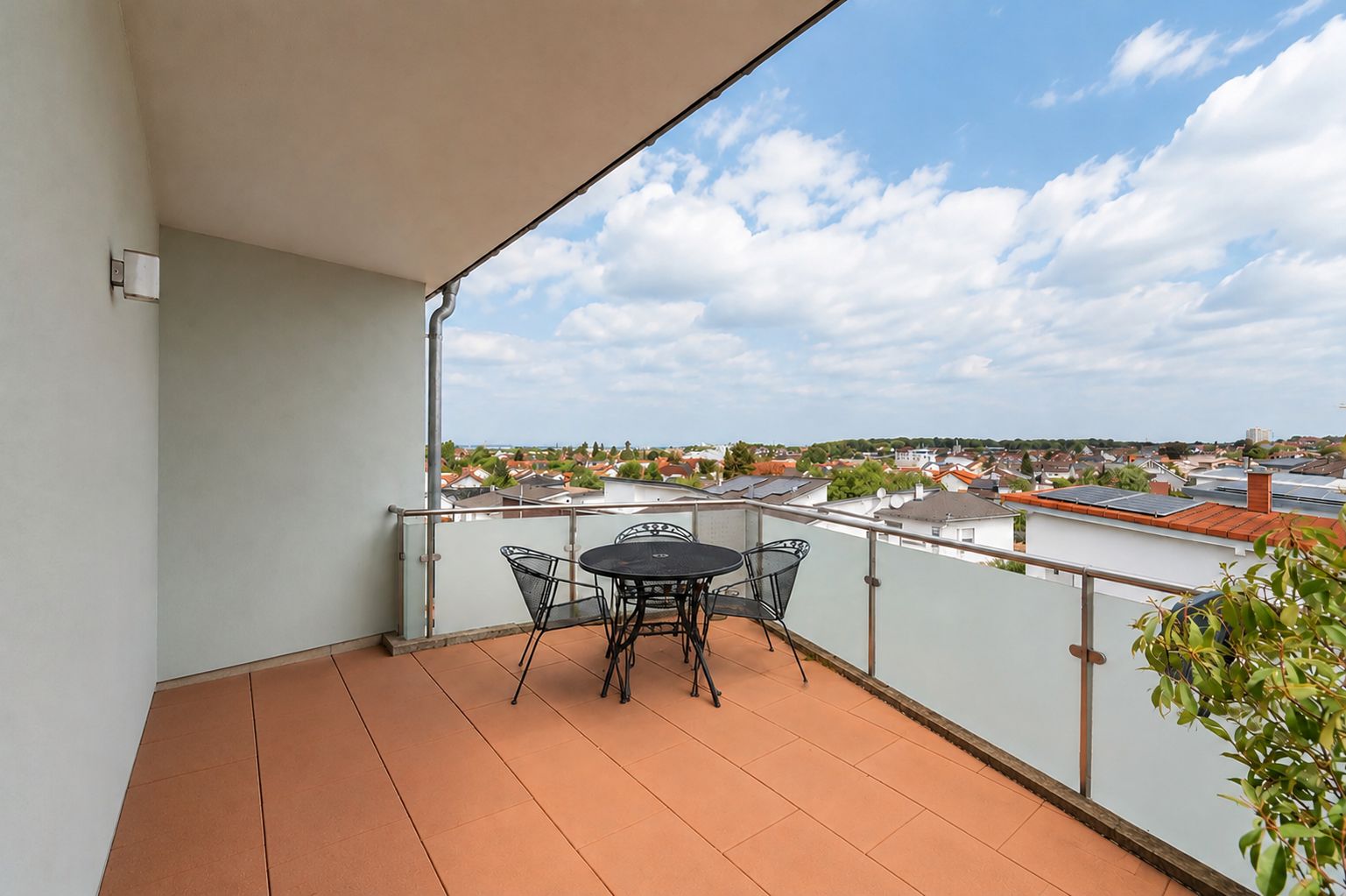 Balkon mit kleinem runden Tisch und vier Stühlen, Blick auf Häuser und blauen Himmel.