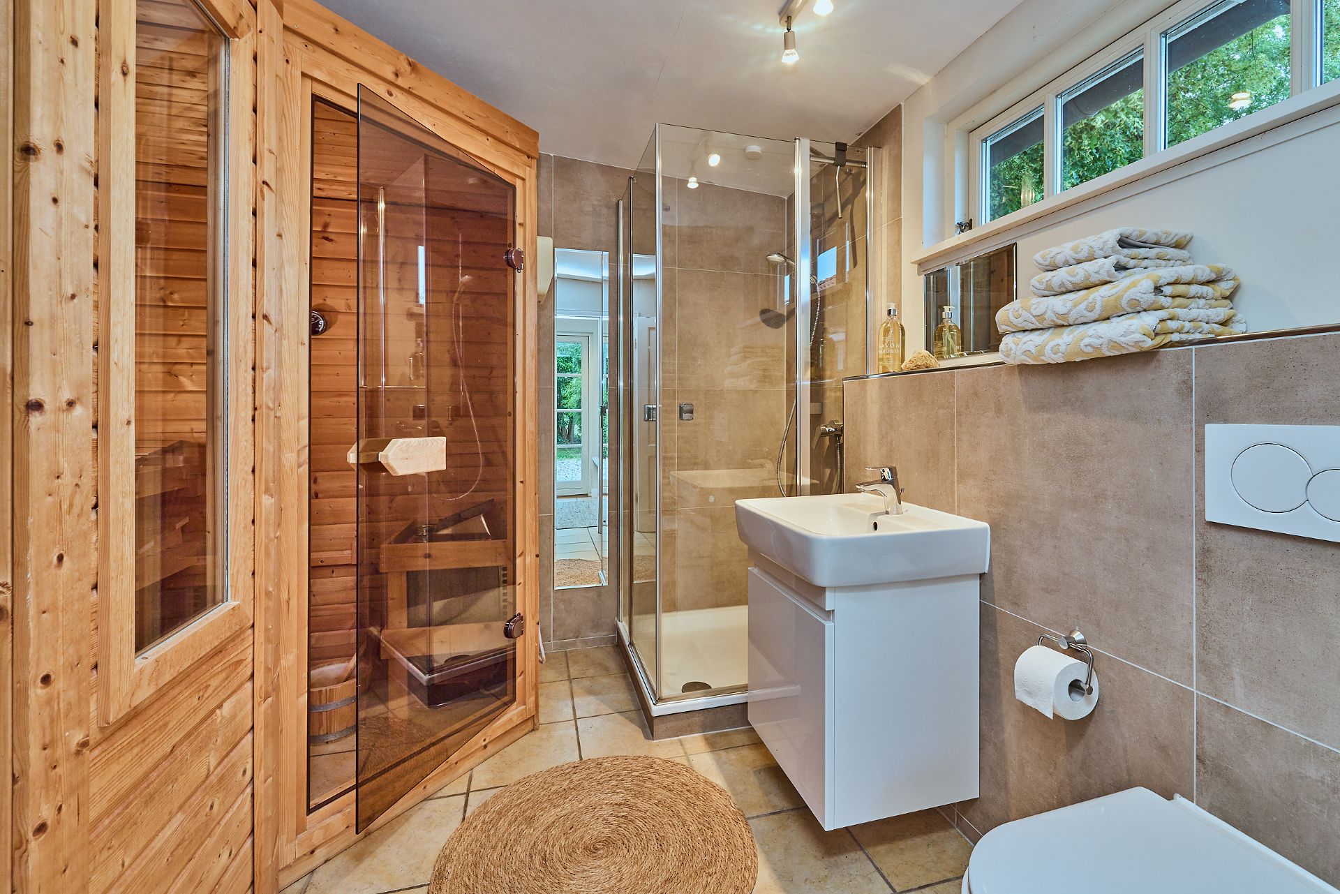 Modernes Badezimmer mit Sauna, Dusche, Waschbecken, WC und gestapelten Handtüchern.