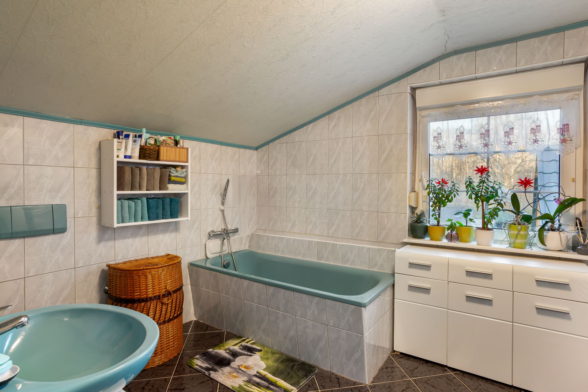 Badezimmer mit blauer Badewanne, Waschbecken, Schrank, Fenster und mehreren Pflanzen auf der Fensterbank.