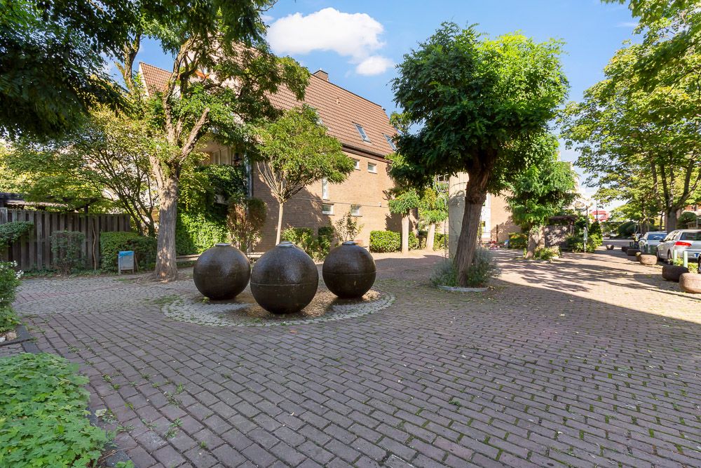 Gepflasterter Innenhof mit drei großen Kugelskulpturen und Bäumen in einer Wohnanlage.