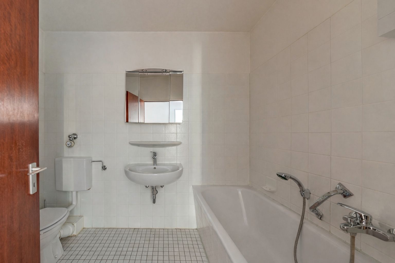 Helles Badezimmer mit Badewanne, Waschbecken, Spiegel und WC, gefliestem Boden und weißen Wänden.