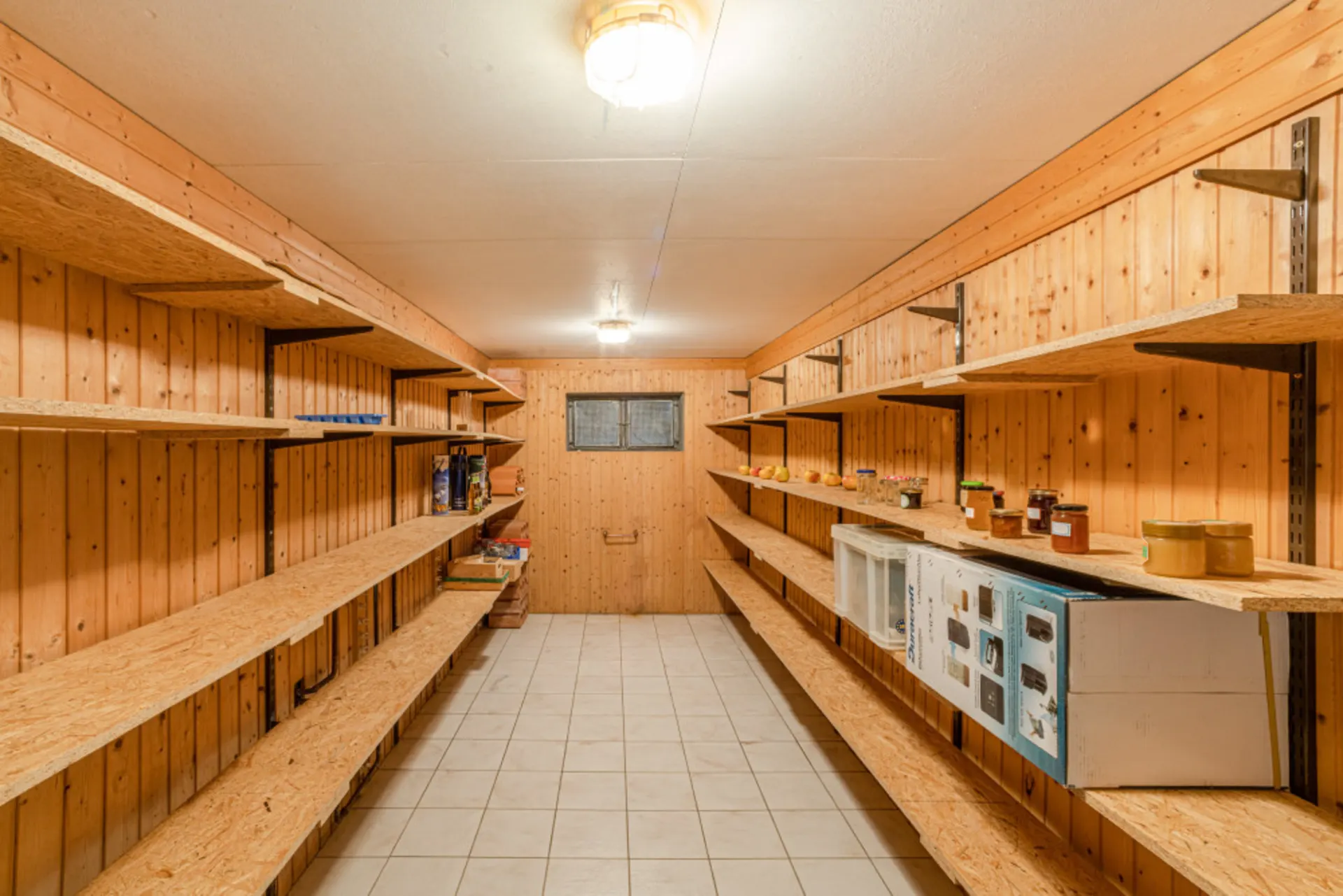 Kellerraum mit Holzregalen an den Wänden, teilweise mit Vorräten und Konserven gefüllt.