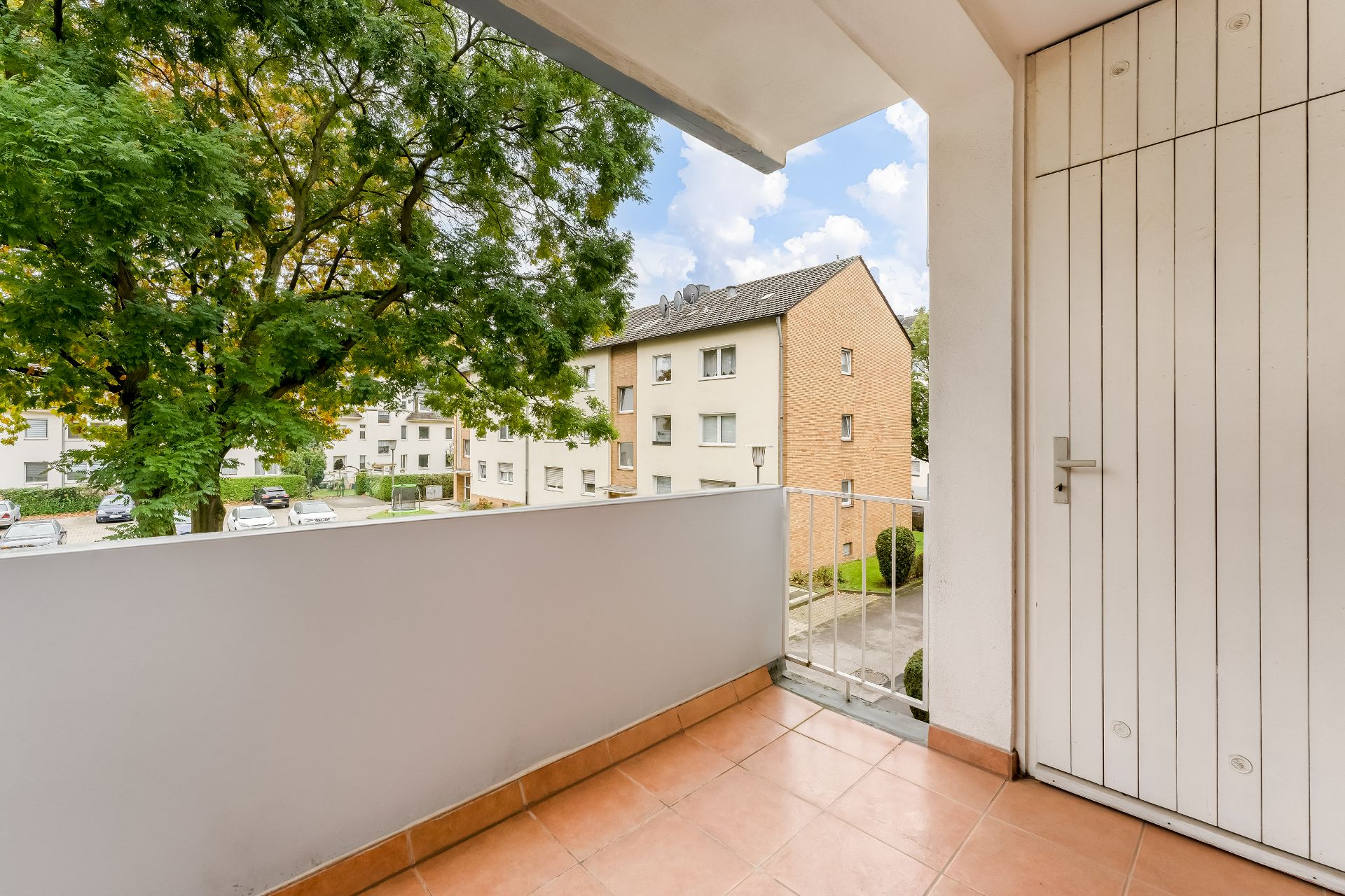 Balkon mit Fliesenboden, Blick auf Baum und Wohngebäude im Hintergrund.