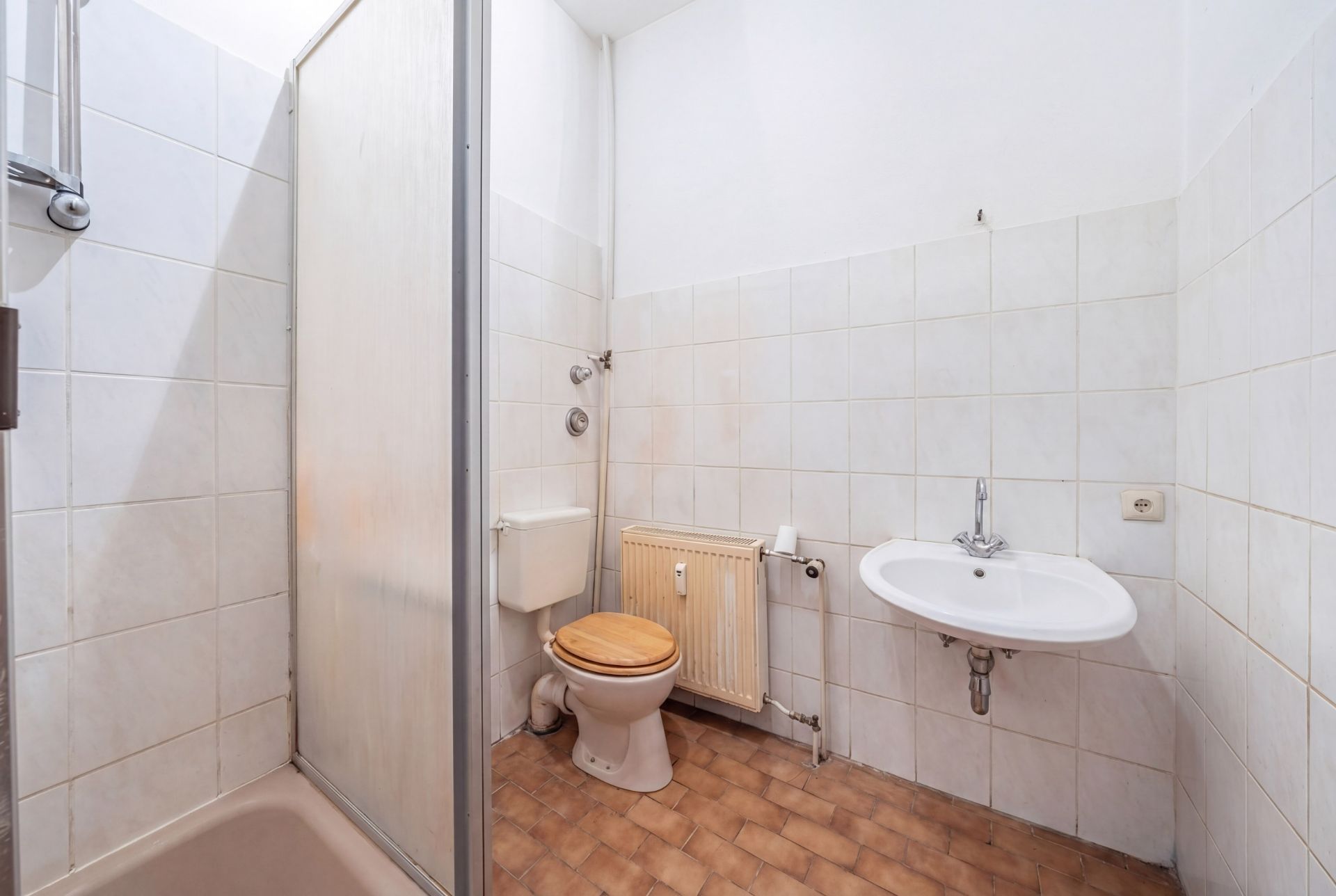 Badezimmer mit Dusche, Toilette mit Holzsitz, Waschbecken und Fliesenboden.