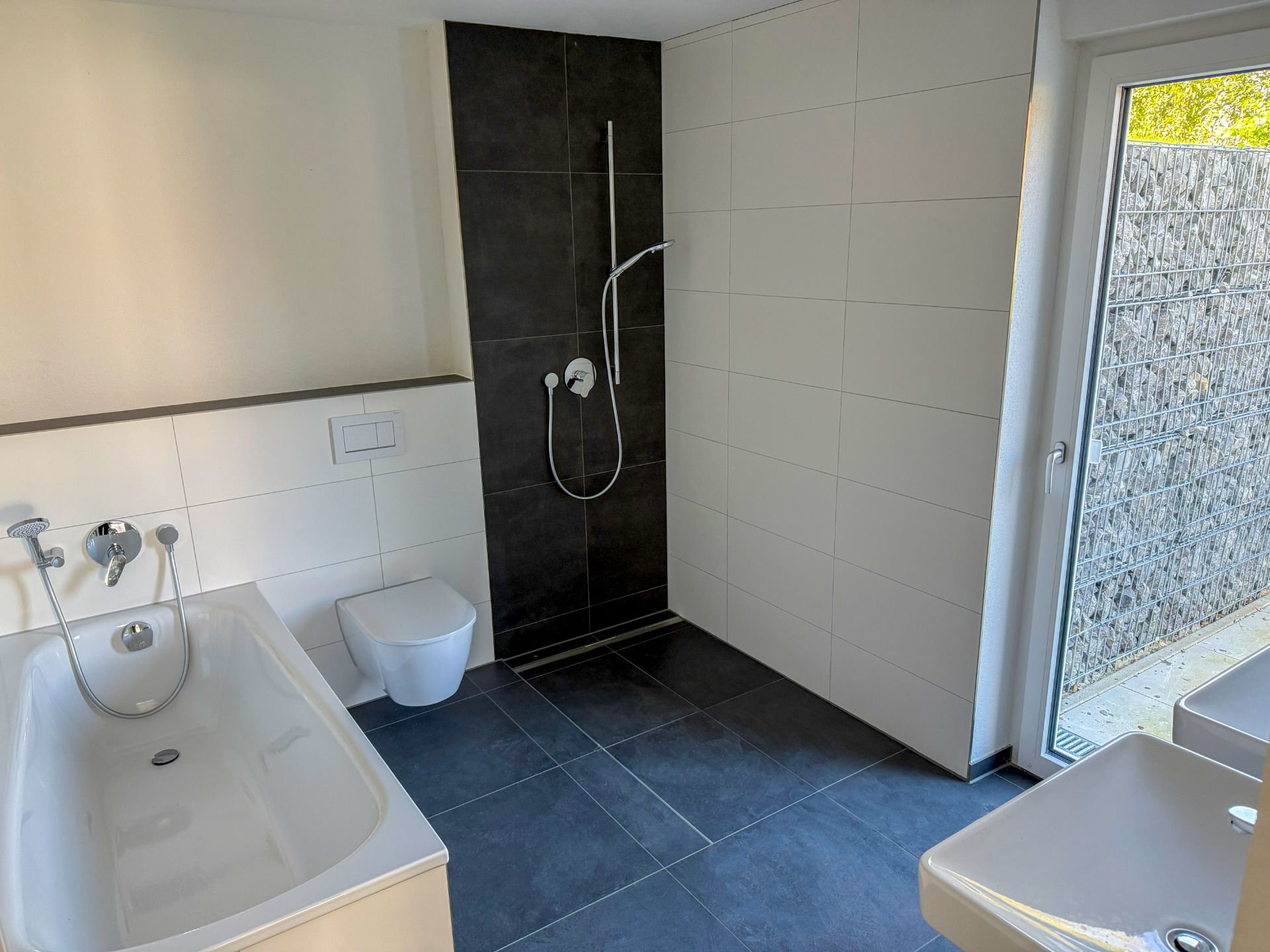 Modernes Badezimmer mit Badewanne, Dusche, WC und großem Fenster.
