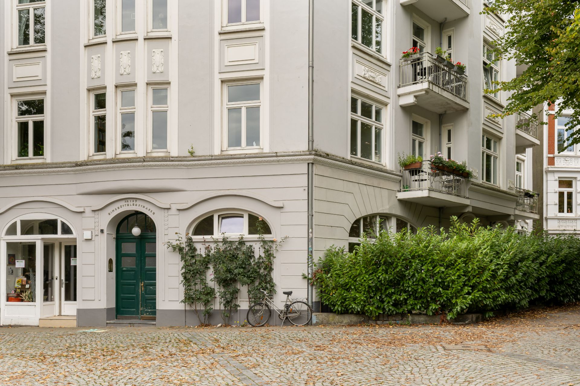Mehrstöckiges Wohnhaus mit Balkonen, grüner Haustür, Fahrrad und Pflanzen am Eingang.
