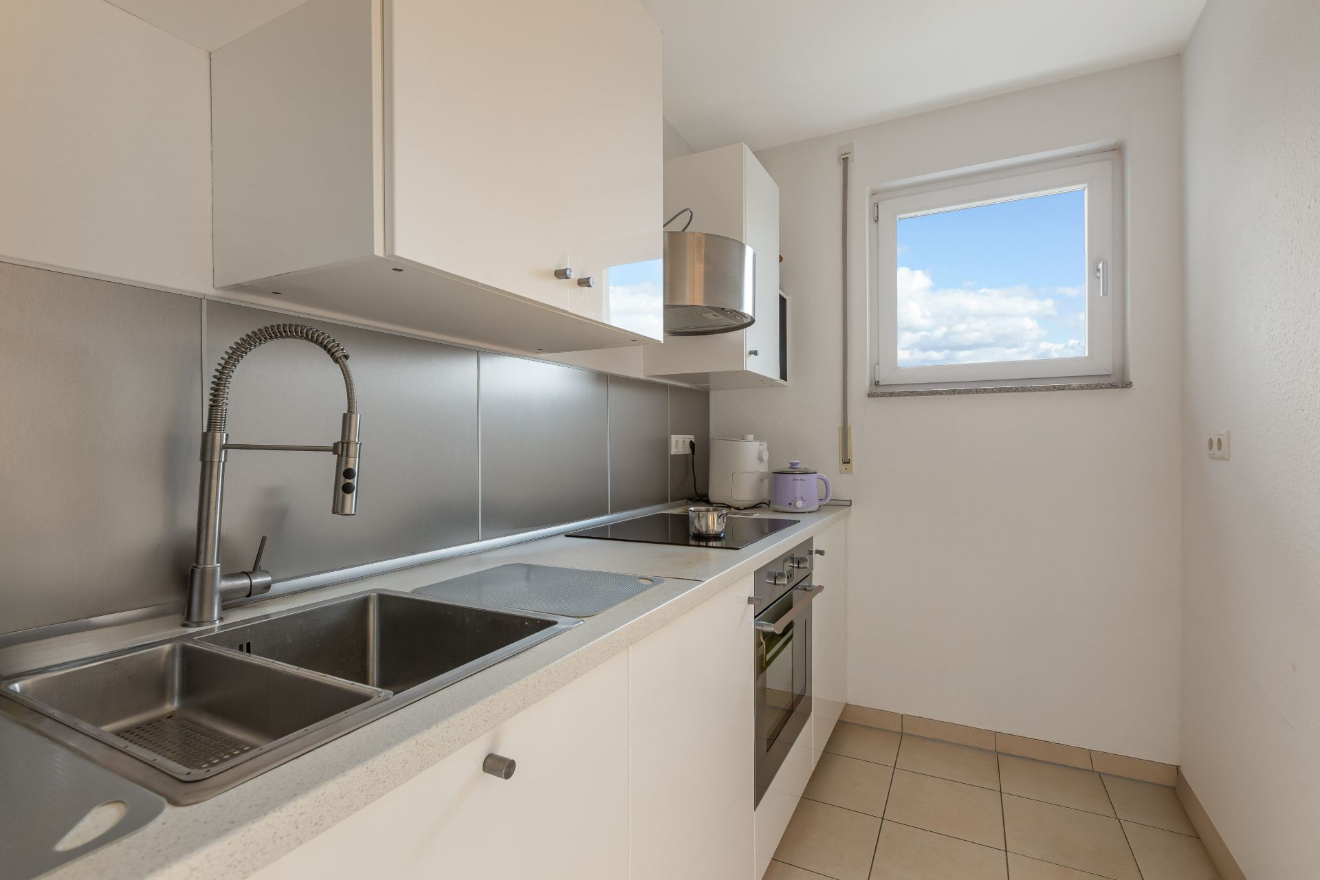 Moderne, kleine Küche mit Doppelspüle, Herd, weißen Schränken und Fenster.
