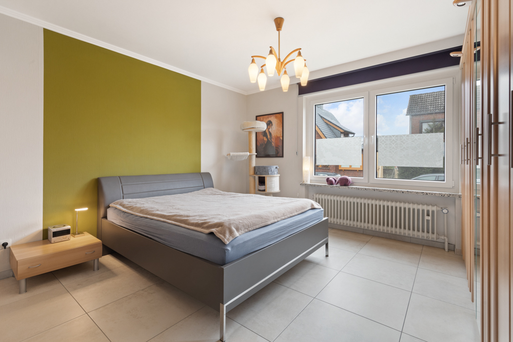 Modernes Schlafzimmer mit Doppelbett, Nachttisch, großem Fenster und Kleiderschrank.