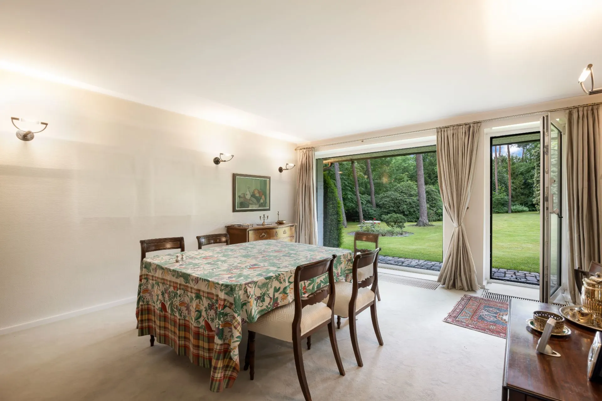 Esszimmer mit großem Tisch, sechs Stühlen und Blick in einen Garten durch offene Glastüren.