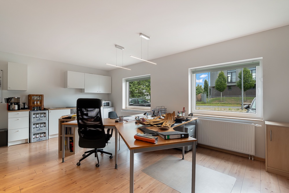 Helles Arbeitszimmer mit zwei Schreibtischen, Stuhl, Regalen und Blick aus zwei Fenstern auf eine Straße.