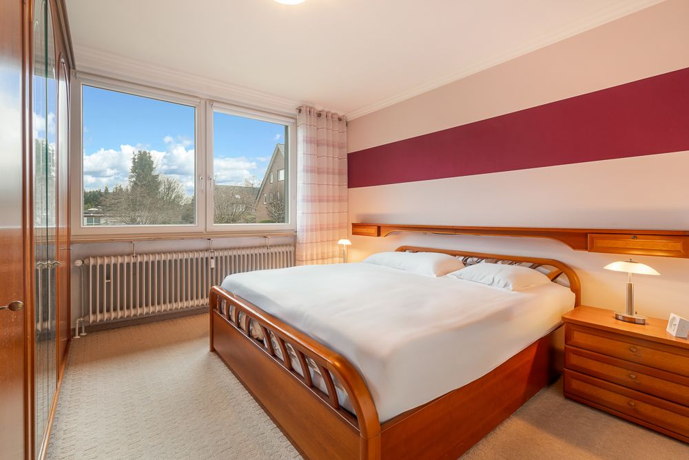 Helles Schlafzimmer mit Doppelbett, Nachttischen, Fenster und großem Kleiderschrank.