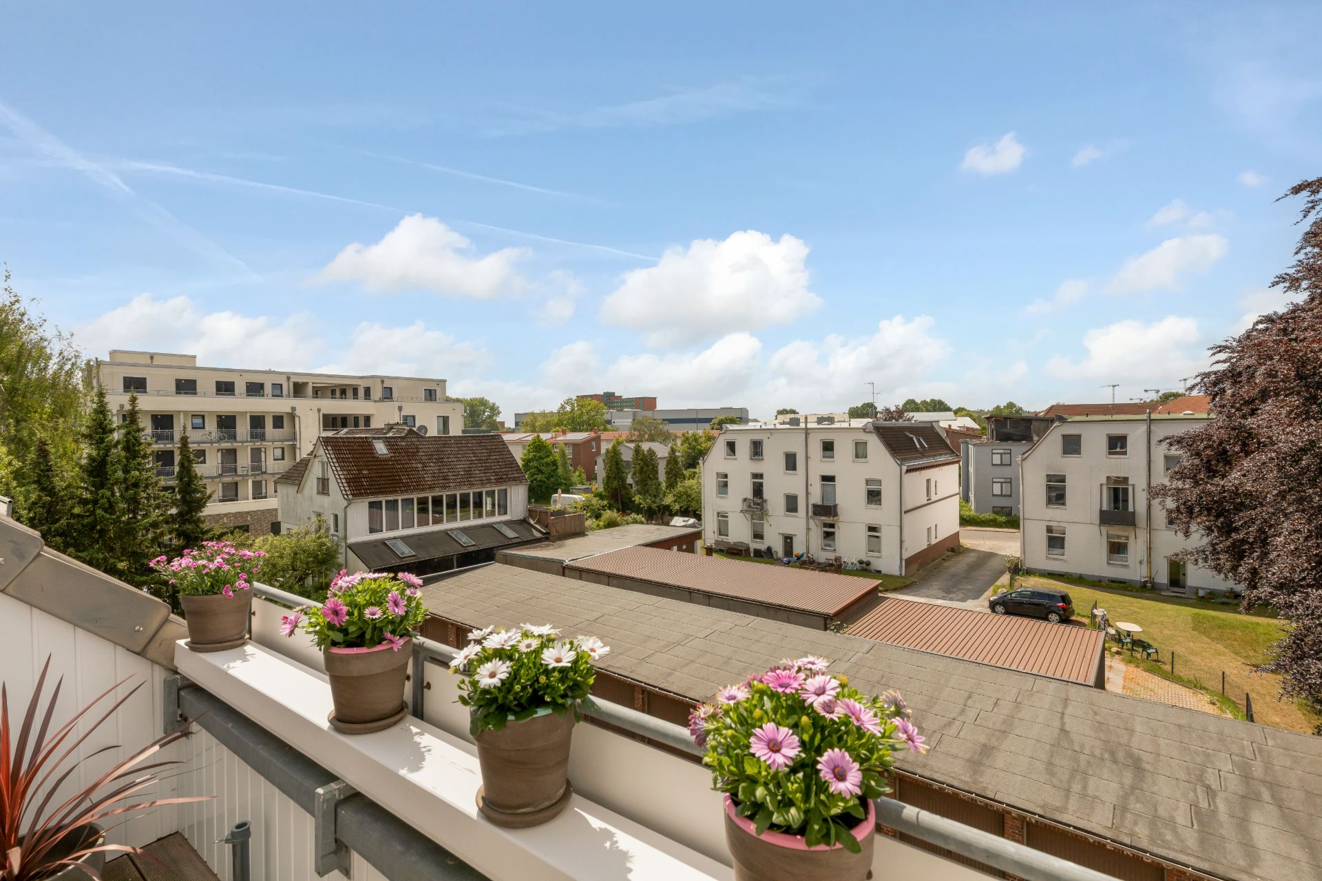 Blick von einem Balkon mit Blumenkästen auf Wohnhäuser und einen Innenhof.