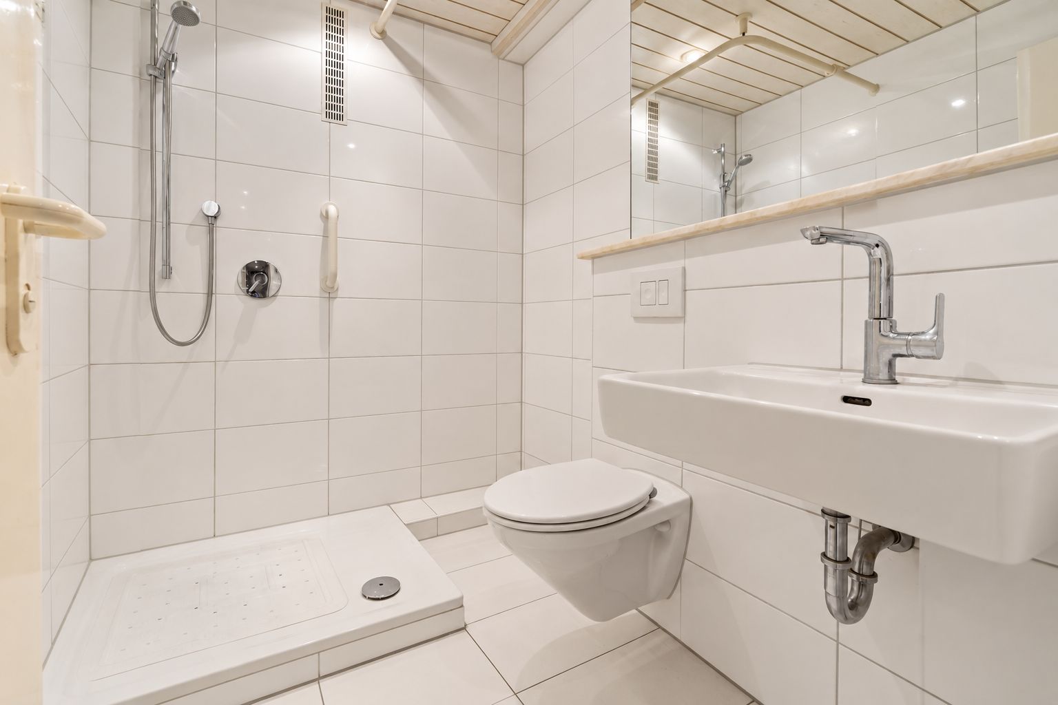 Helles, modernes Bad mit Dusche, Wandtoilette, Waschbecken und großem Spiegel.