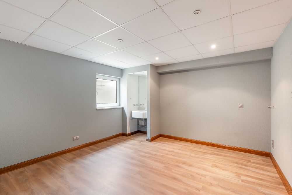 Leerer Raum mit Holzfußboden, grauen Wänden, Fenster und kleinem Waschbecken in einer Nische.