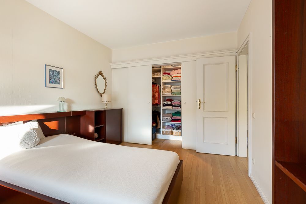 Schlafzimmer mit Holzboden, Bett, Regal und offenem Kleiderschrank mit gefalteter Kleidung.