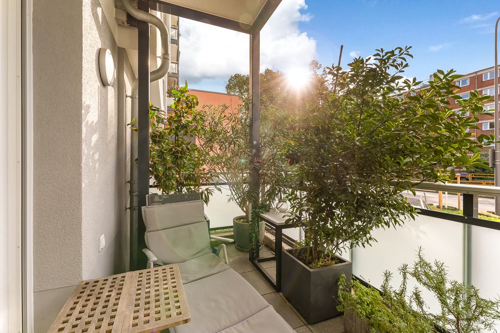 Balkon mit Liegestuhl, kleinem Tisch und mehreren großen Pflanzen in Töpfen.