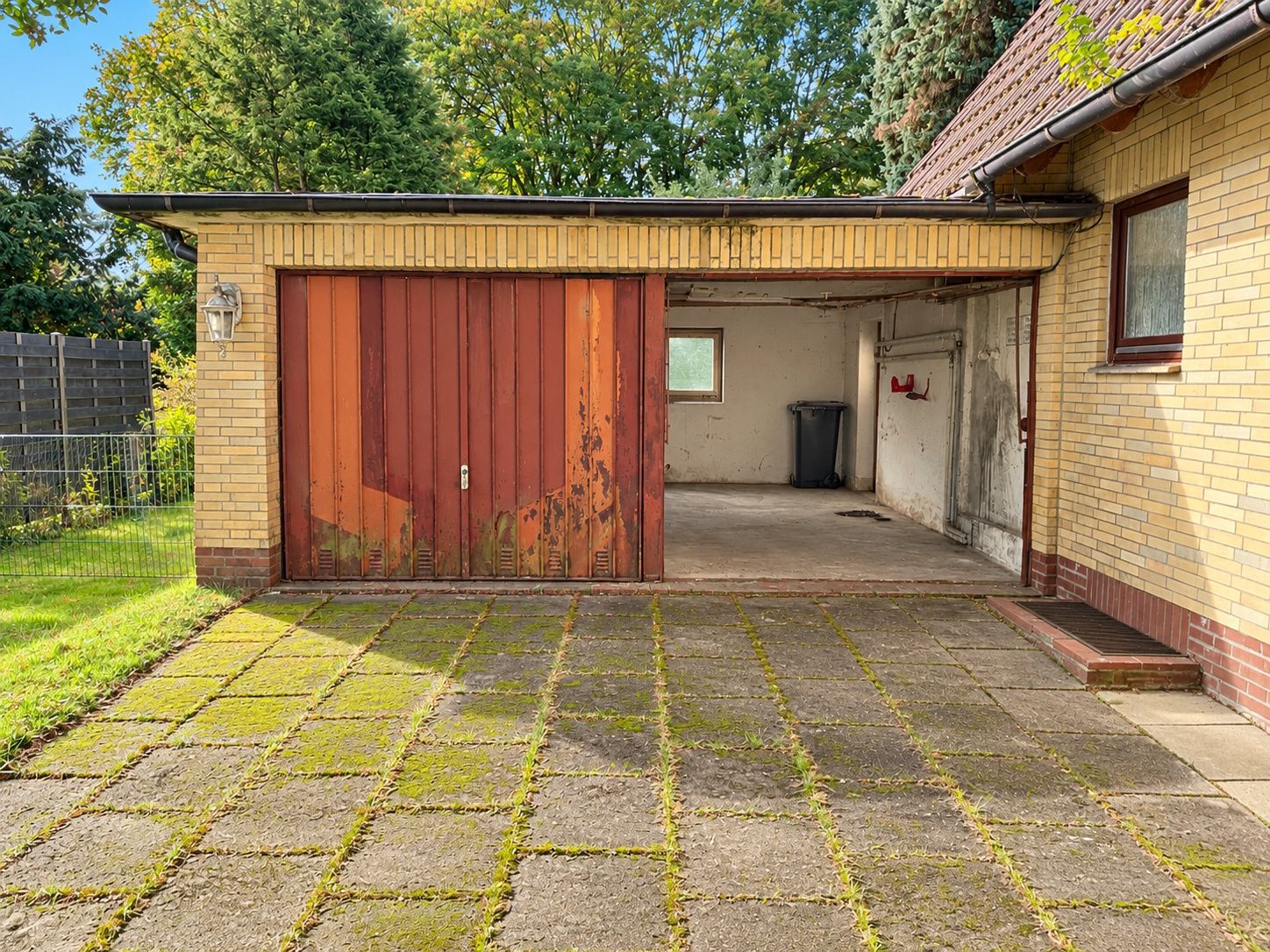 Garage mit teilweise geöffneter roter Tür und großem gepflastertem Hof davor.