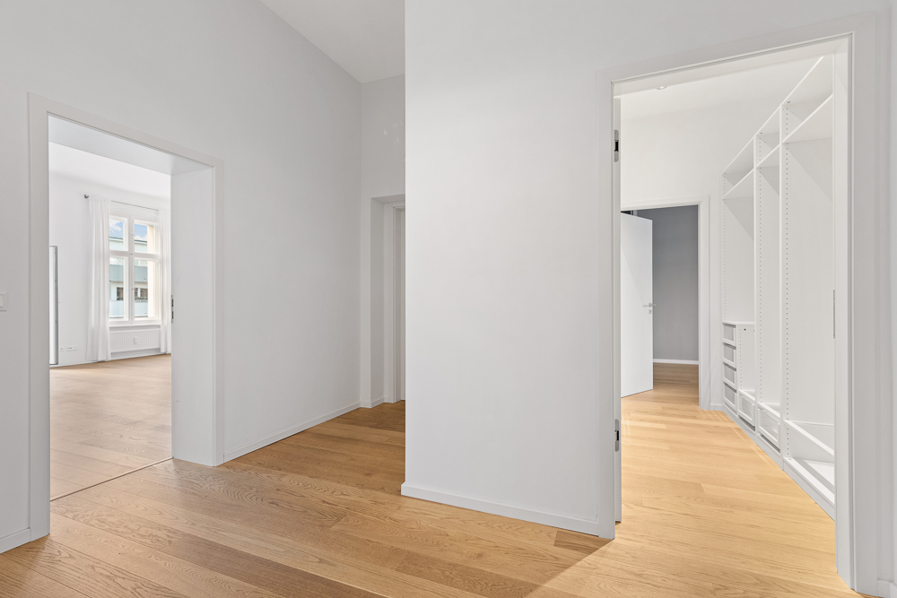 Heller Flur mit Holzboden, Zugang zu Zimmer und begehbarem Kleiderschrank, weiße Wände.