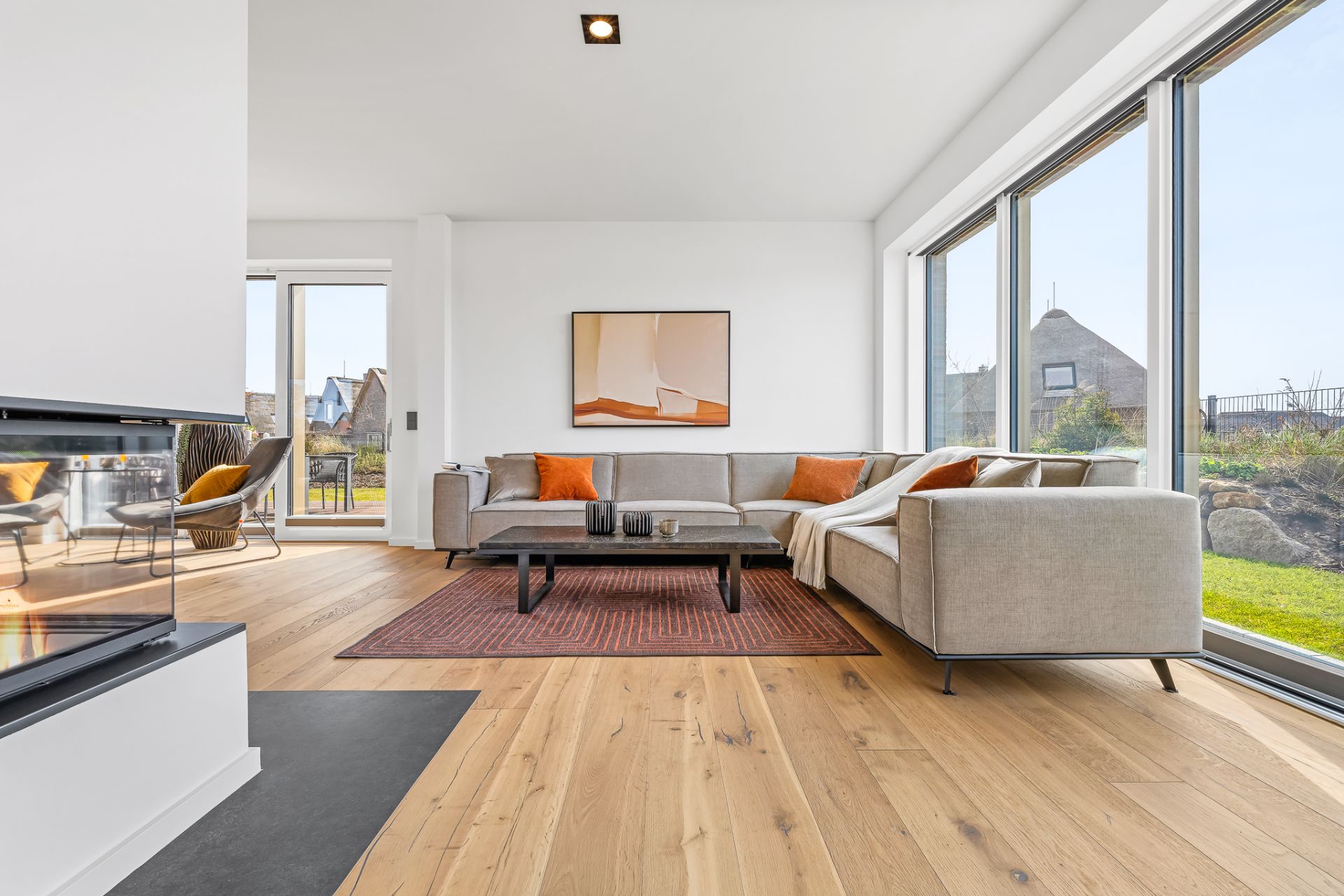 Helles Wohnzimmer mit Ecksofa, Couchtisch, großem Fenster und Parkettboden.