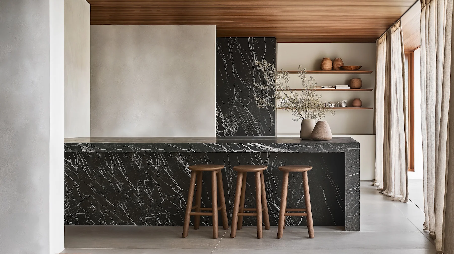 Moderne Küche mit schwarzer Marmorinsel, drei Holzhockern und offenen Regalen mit Keramik.