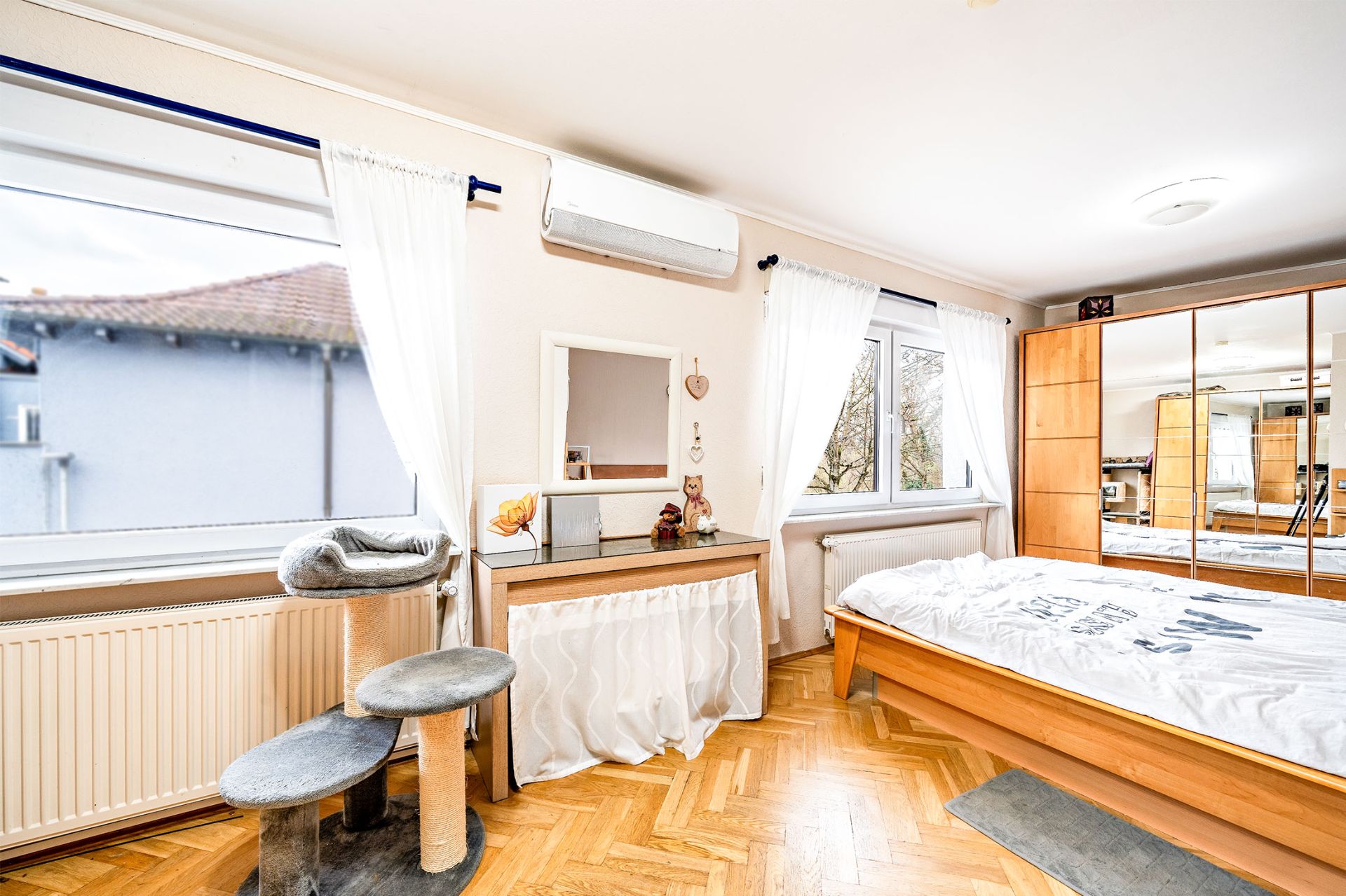Helles Schlafzimmer mit Holzbett, Schminktisch, Kratzbaum und großem Spiegelschrank.