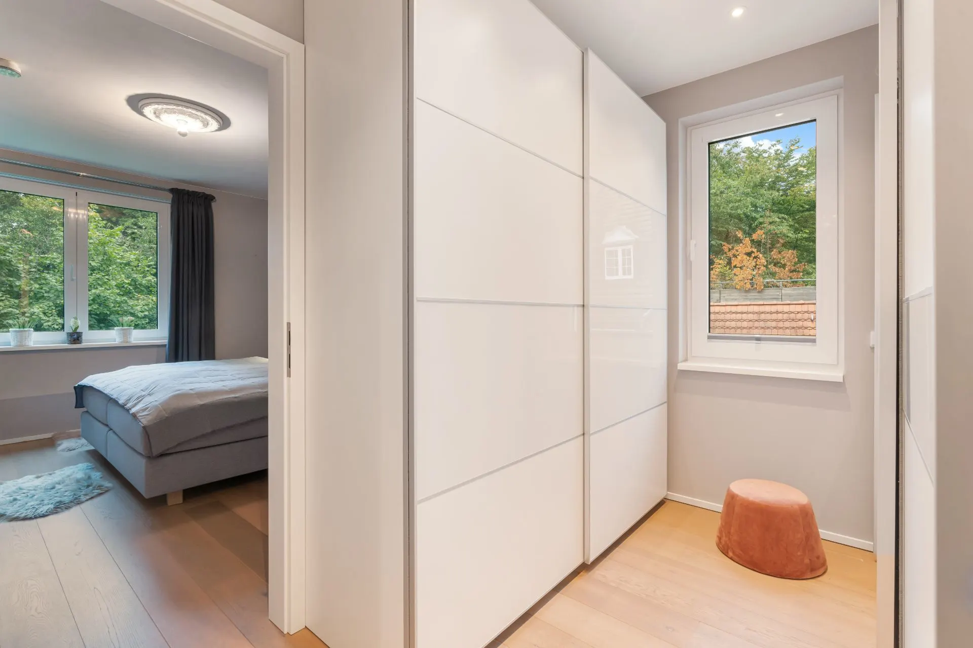 Heller Flur mit großem weißen Schrank, Fenster und Blick ins Schlafzimmer mit Doppelbett.