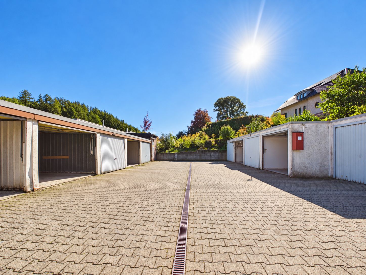 Offener Garagenhof mit mehreren Einzelgaragen und Pflastersteinen bei Sonnenschein.
