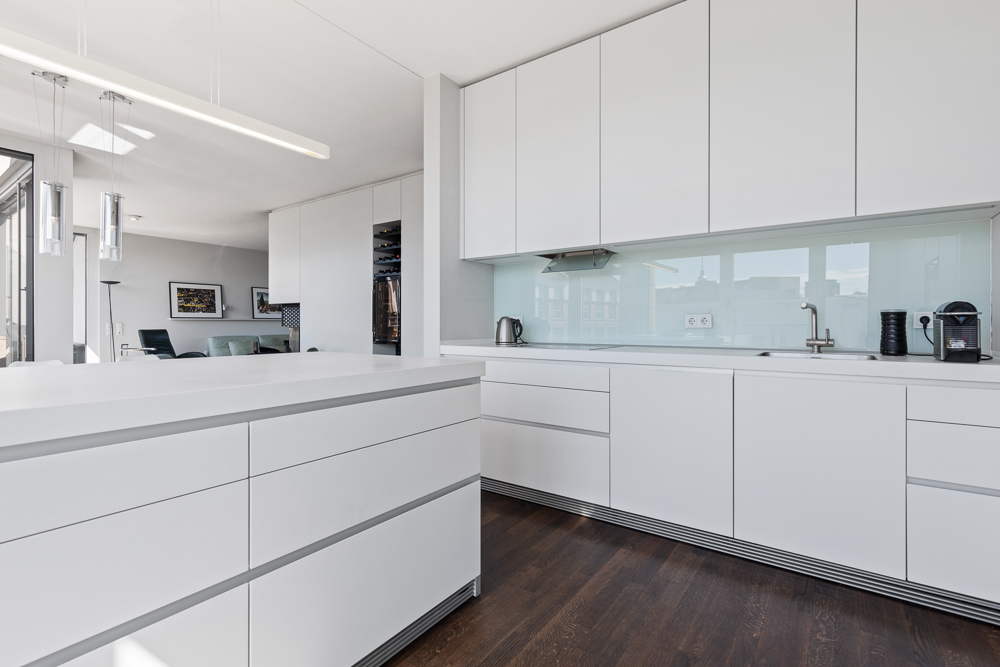 Moderne weiße Einbauküche mit Hochglanzfronten und dunklem Holzboden.