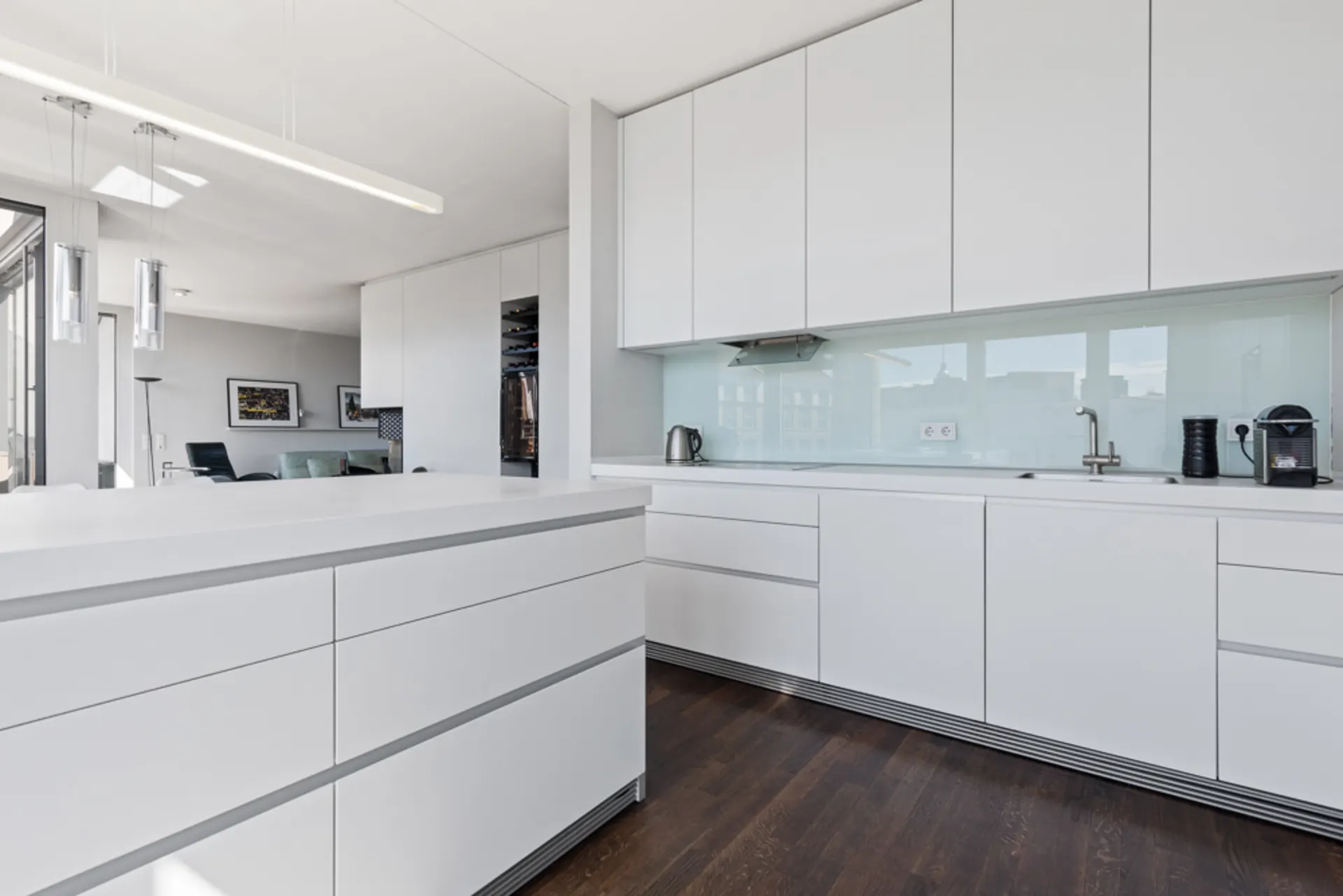 Moderne weiße Einbauküche mit Hochglanzfronten und dunklem Holzboden.