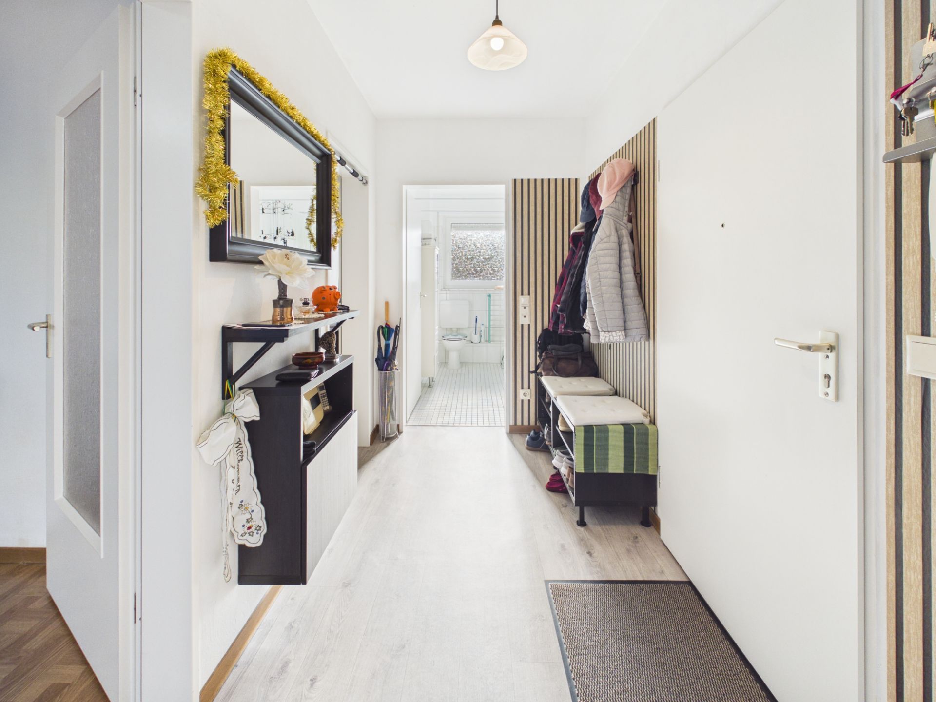 Heller Flur mit Spiegel, Regal, Garderobe und Blick ins Badezimmer.