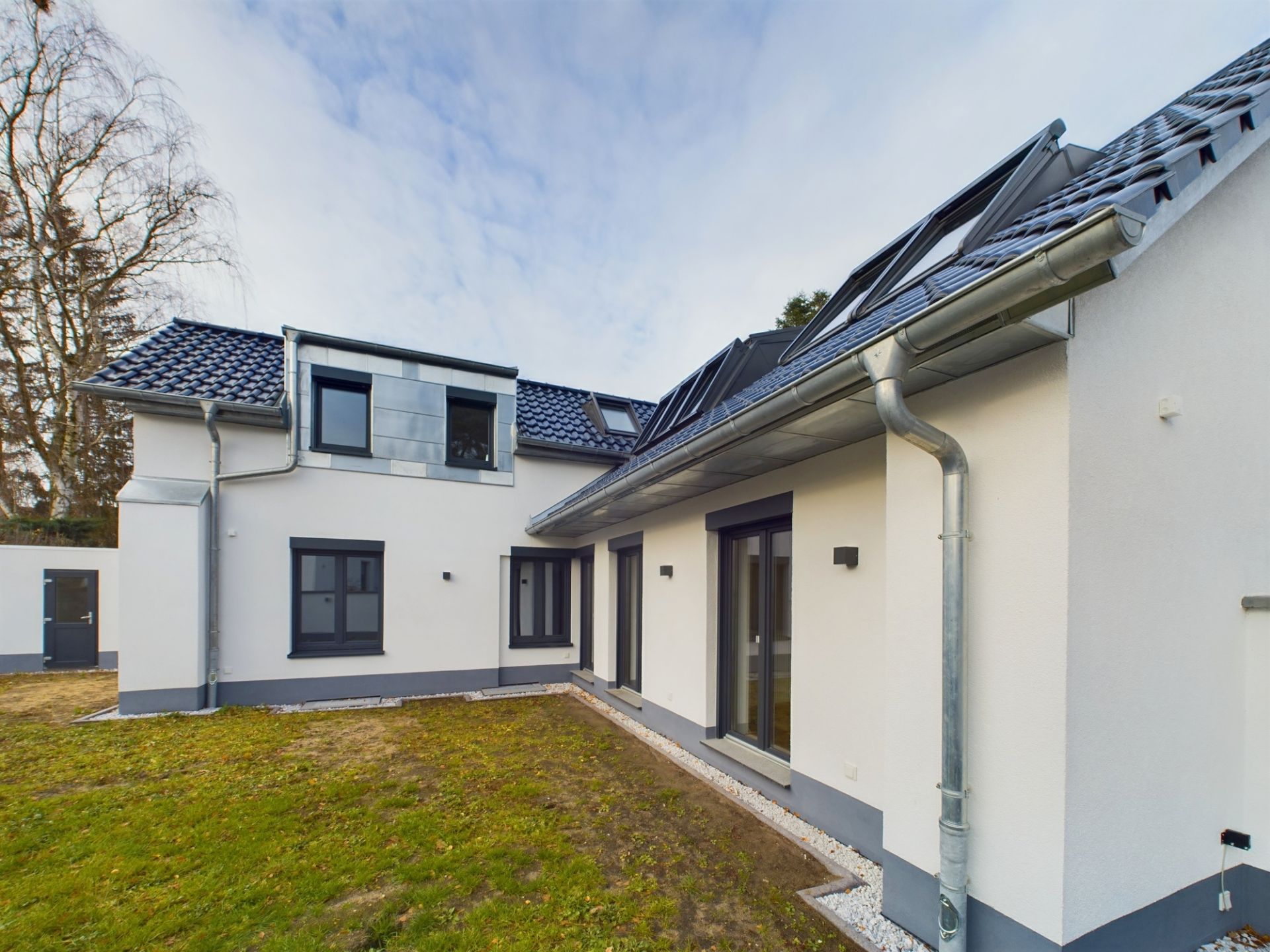 Moderner weißer Wohnhausanbau mit mehreren Fenstern und kleinem Garten im Vordergrund.