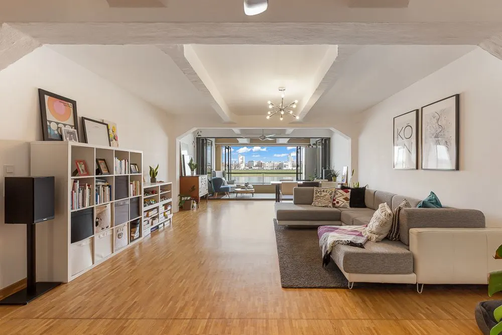 Geräumiges Wohnzimmer mit Holzboden, Sofa, Bücherregal und großem Fenster mit Stadtblick.