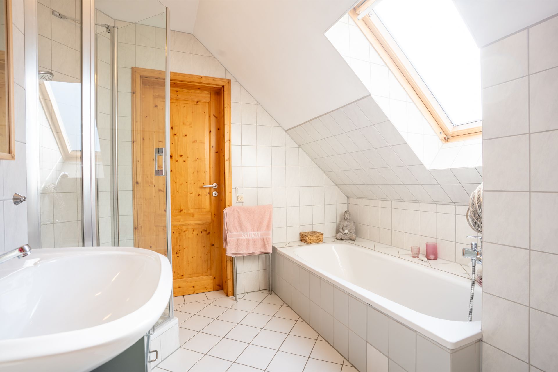 Helles Badezimmer mit Badewanne, Waschbecken, Dachfenster und Holz-Tür.
