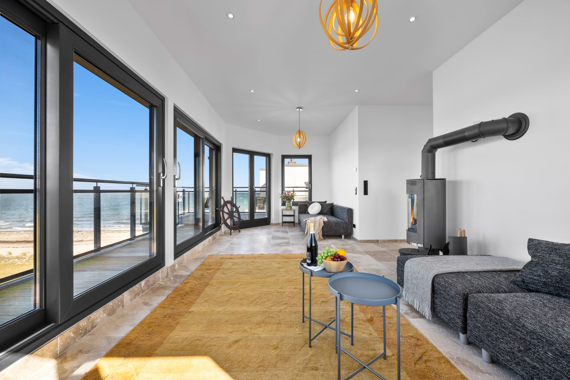 Modernes Wohnzimmer mit großen Fenstern, Meerblick, Sofa, Kamin und gelbem Teppich.