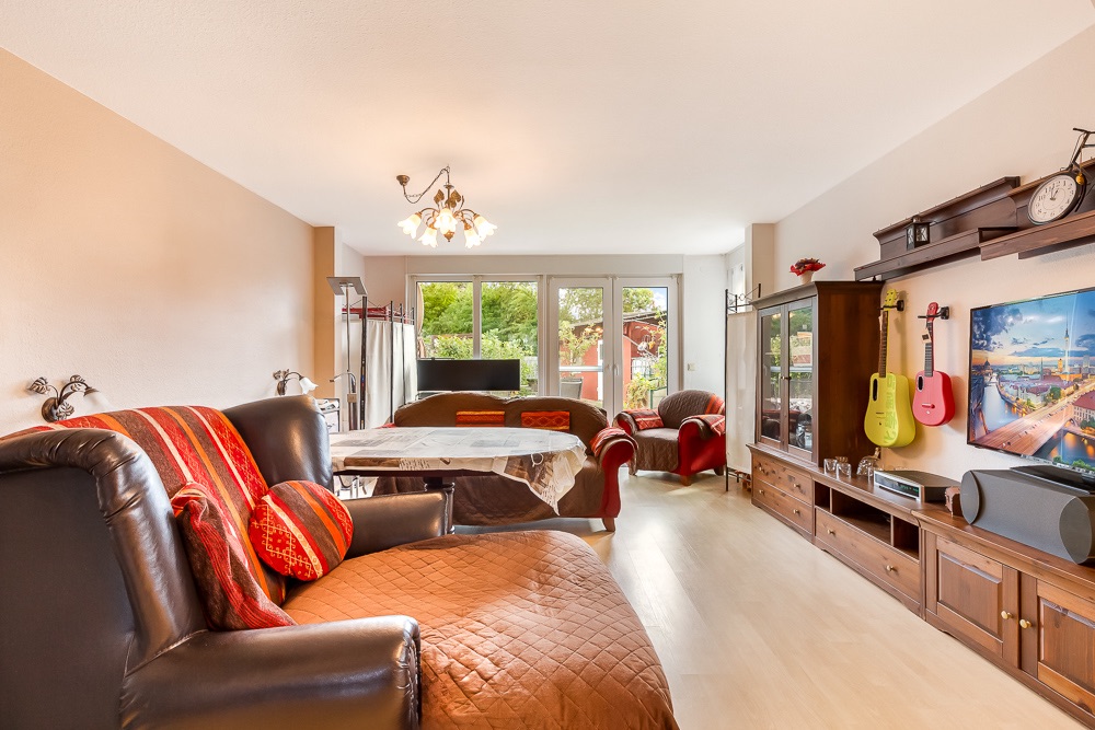Wohnzimmer mit Ledersessel, Esstisch, TV, Gitarren an der Wand und großen Fenstern zum Garten.