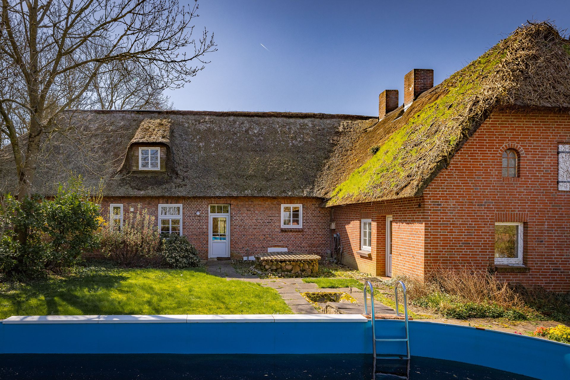 Backsteinhaus mit Reetdach, Garten und rundem Pool im Vordergrund.