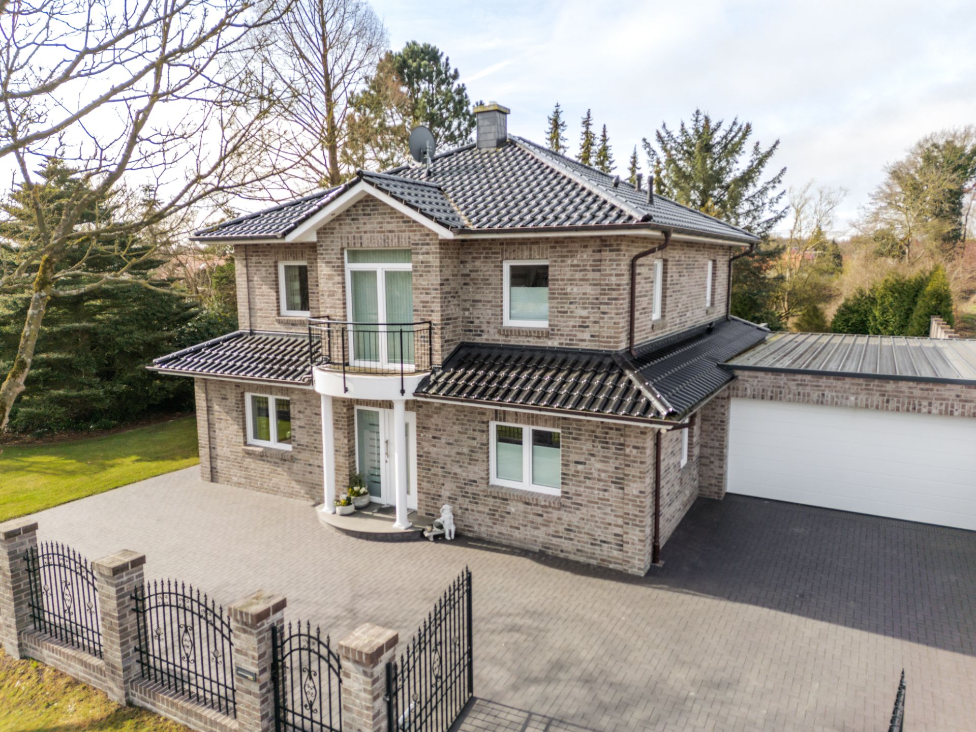 Modernes zweistöckiges Backsteinhaus mit schwarzem Dach und Doppelgarage, umzäunt.