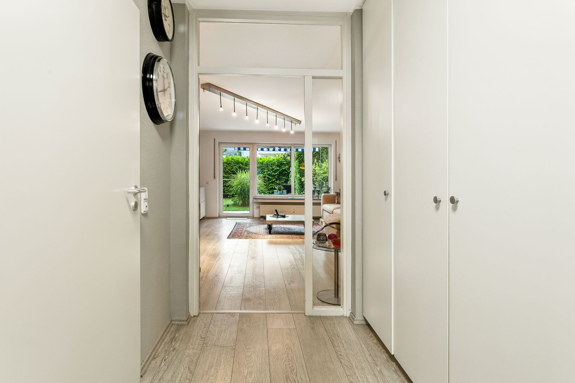 Heller Flur mit Holzboden, weißen Wandschränken und Blick ins Wohnzimmer mit großen Fenstern.