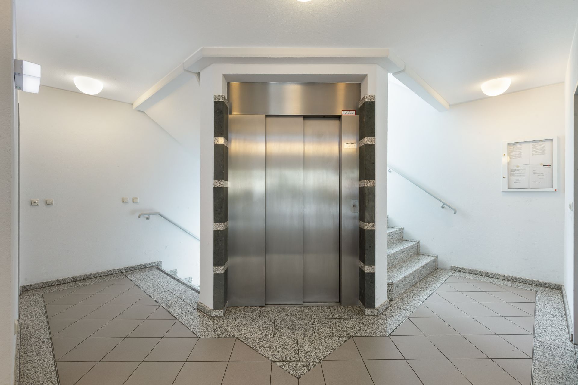 Heller Flur mit Aufzug in der Mitte und Treppen auf beiden Seiten.