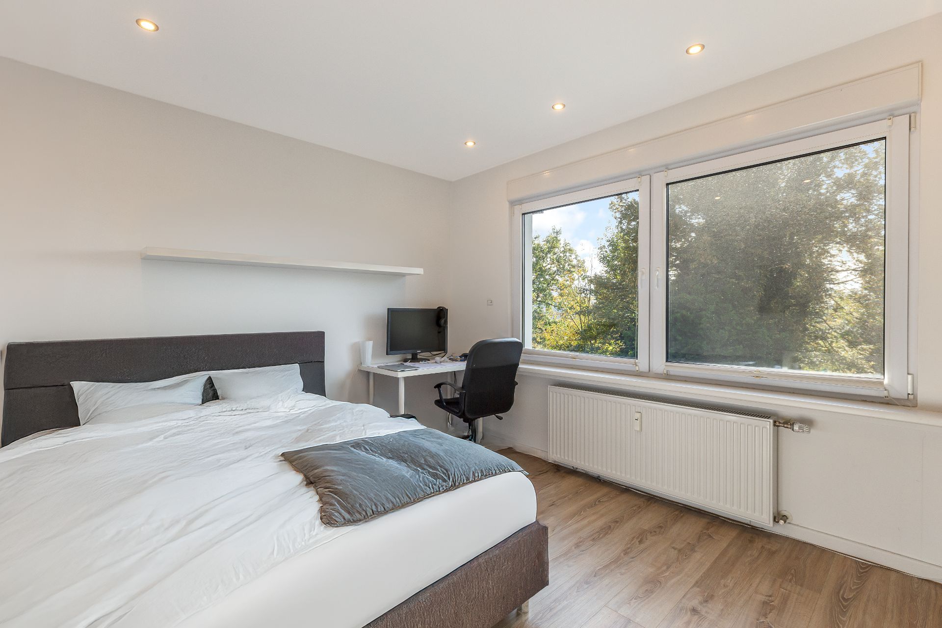 Helles Schlafzimmer mit Bett, Schreibtisch und großem Fenster mit Blick ins Grüne.