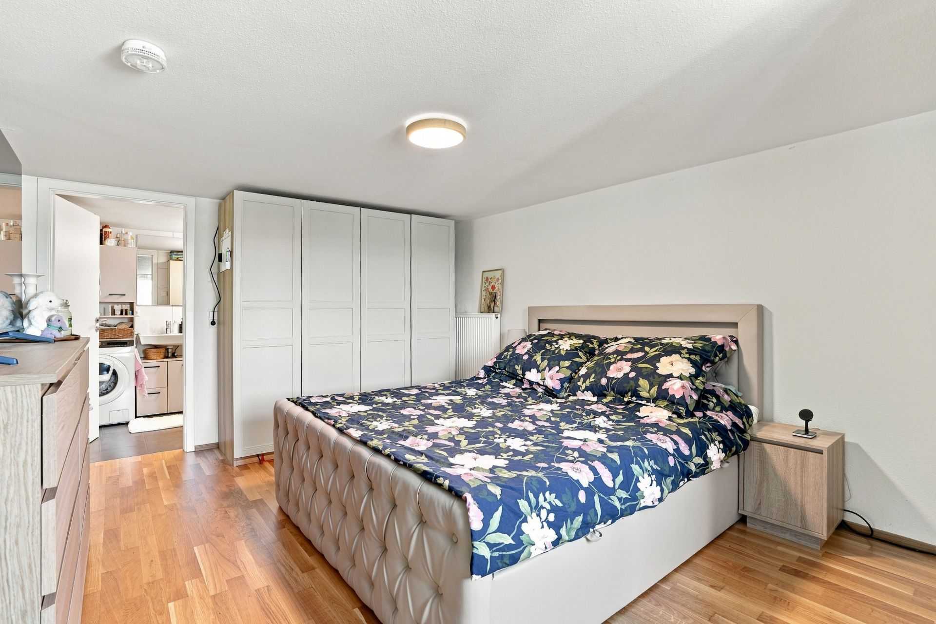 Schlafzimmer mit Doppelbett, floralem Bettbezug, Kleiderschrank und Nachttisch auf Holzfußboden.