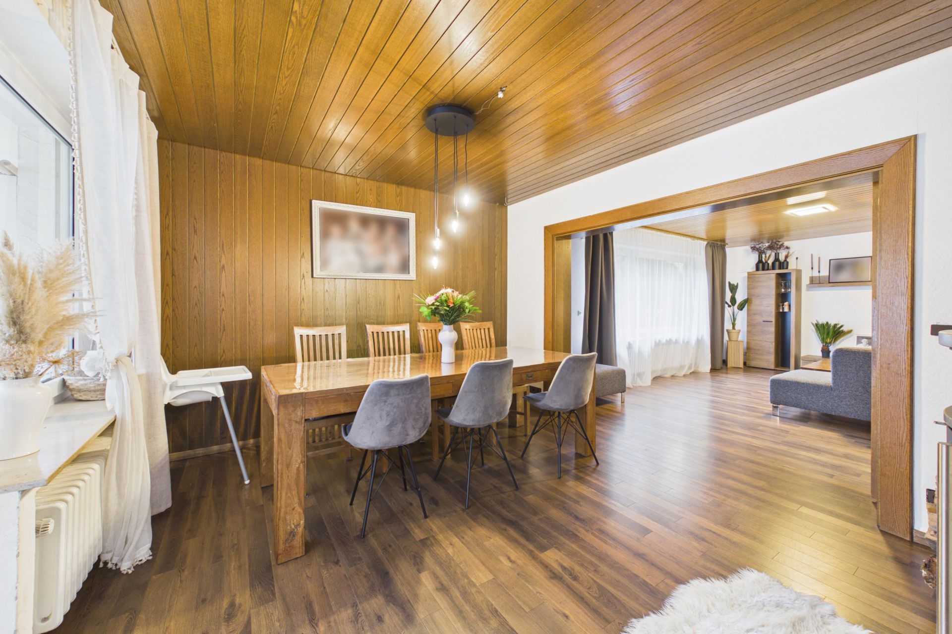 Essbereich mit Holztisch, sechs Stühlen, Holzdecke und Blick ins Wohnzimmer mit Sofa.