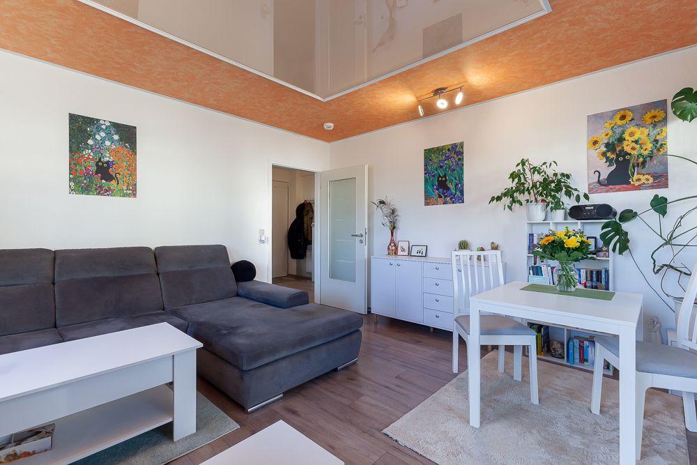 Helles Wohnzimmer mit grauem Sofa, weißem Tisch, Essbereich und Pflanzen an den Wänden.