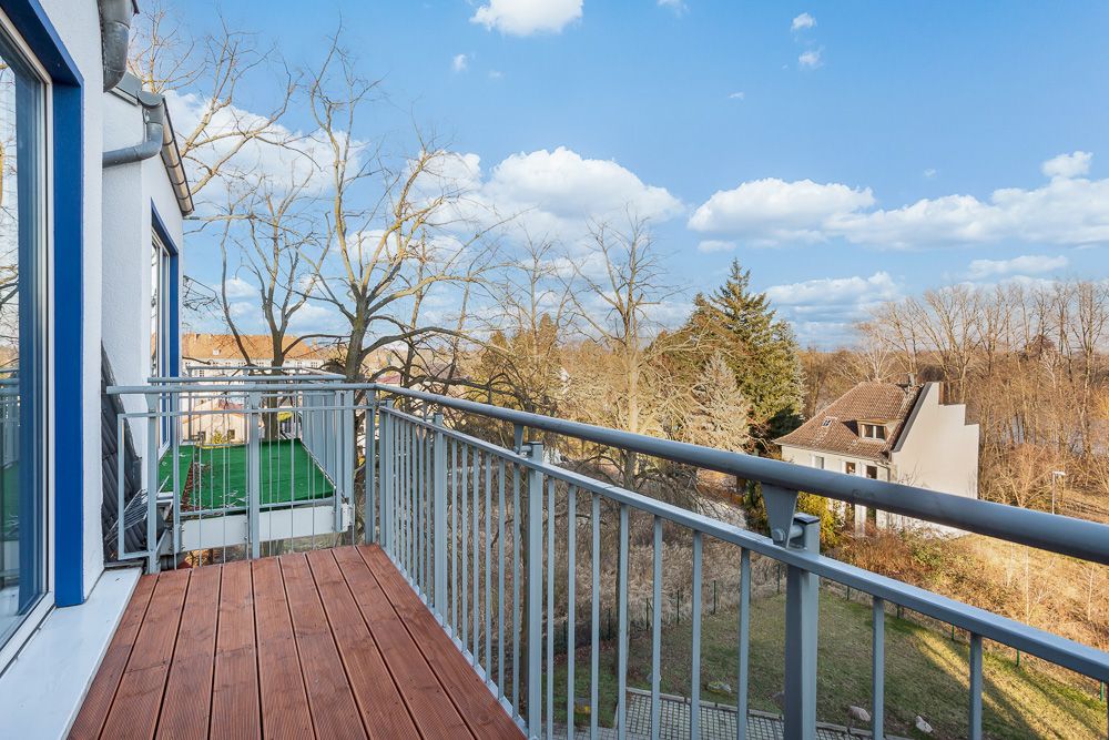 Balkon mit Holzfußboden und Metallgeländer, Blick auf Garten und Bäume.