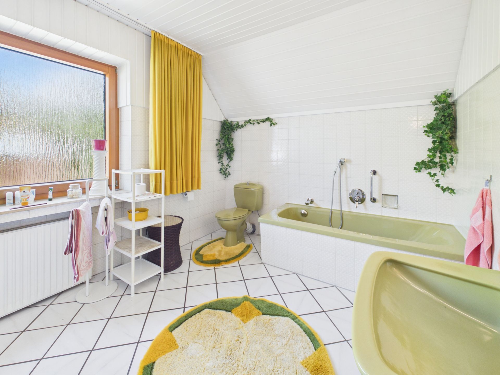 Badezimmer mit grüner Badewanne, WC, Waschtisch, gelben Vorhängen und weißen Fliesen.