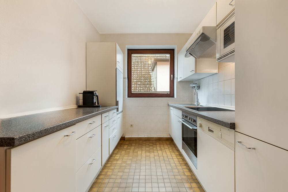 Helle Einbauküche mit weißen Schränken, Elektrogeräten und Fenster über der Spüle.