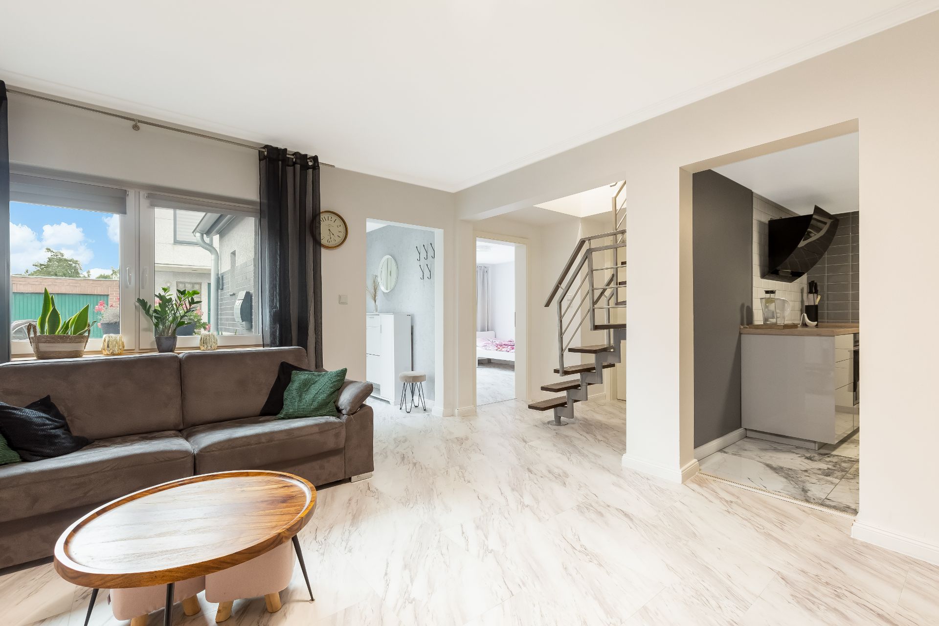 Helles Wohnzimmer mit Sofa, Couchtisch, Pflanzendekoration und moderner Treppe.