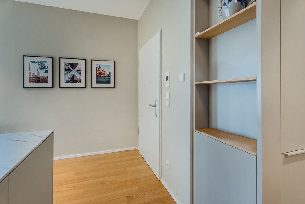 Flur mit Holzboden, drei gerahmten Bildern an der Wand und offenem Regal mit Vase.